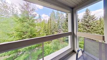 A room with a large window offering a view of dense green trees and a clear sky.