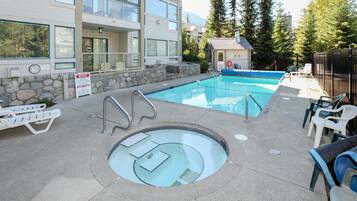 A swimming pool with a hot tub, lounge chairs, and a stone wall.