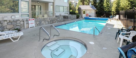 Una piscina con hidromasaje, sillas de descanso y un muro de piedra.