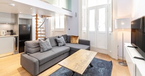 Ein moderner Wohnbereich mit grauem Sofa, einem Holztisch und einer Küchenzeile mit Kühlschrank und Herd.