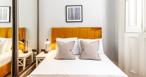 Ein Hotelzimmer mit einem Bett, Nachttischlampen, einem gerahmten Bild an der Wand und einem Spiegel, der einen Teil des Raumes reflektiert.