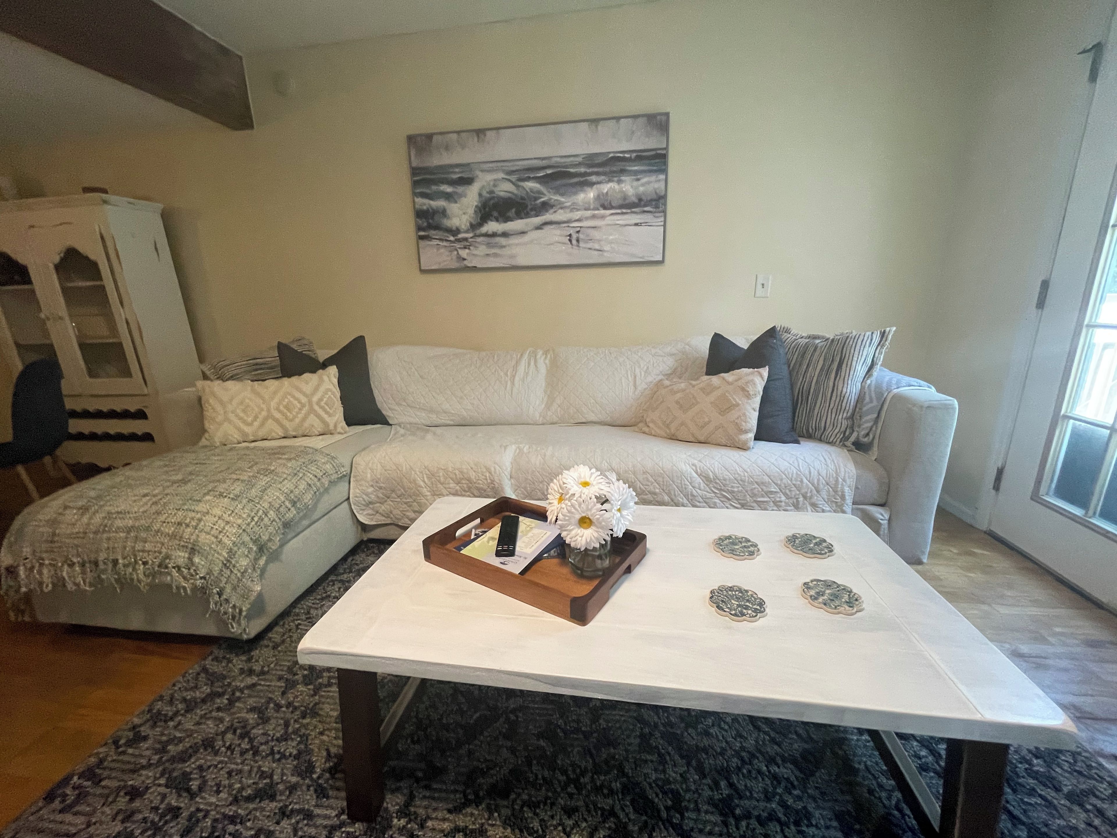 Un salon avec un canapé blanc, une table basse agrémentée d’objets décoratifs, un tableau au mur et une fenêtre laissant entrer la lumière naturelle.