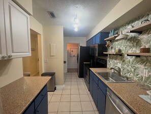 A kitchen with blue cabinets, a stainless steel sink, and a tiled floor. - Cozy 2-bedroom condo on St. Simons Island (St. Simons Island)
