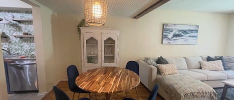 Un comedor con una mesa redonda de madera y sillas azules, un armario blanco con puertas de cristal, y un sofá blanco con cojines.