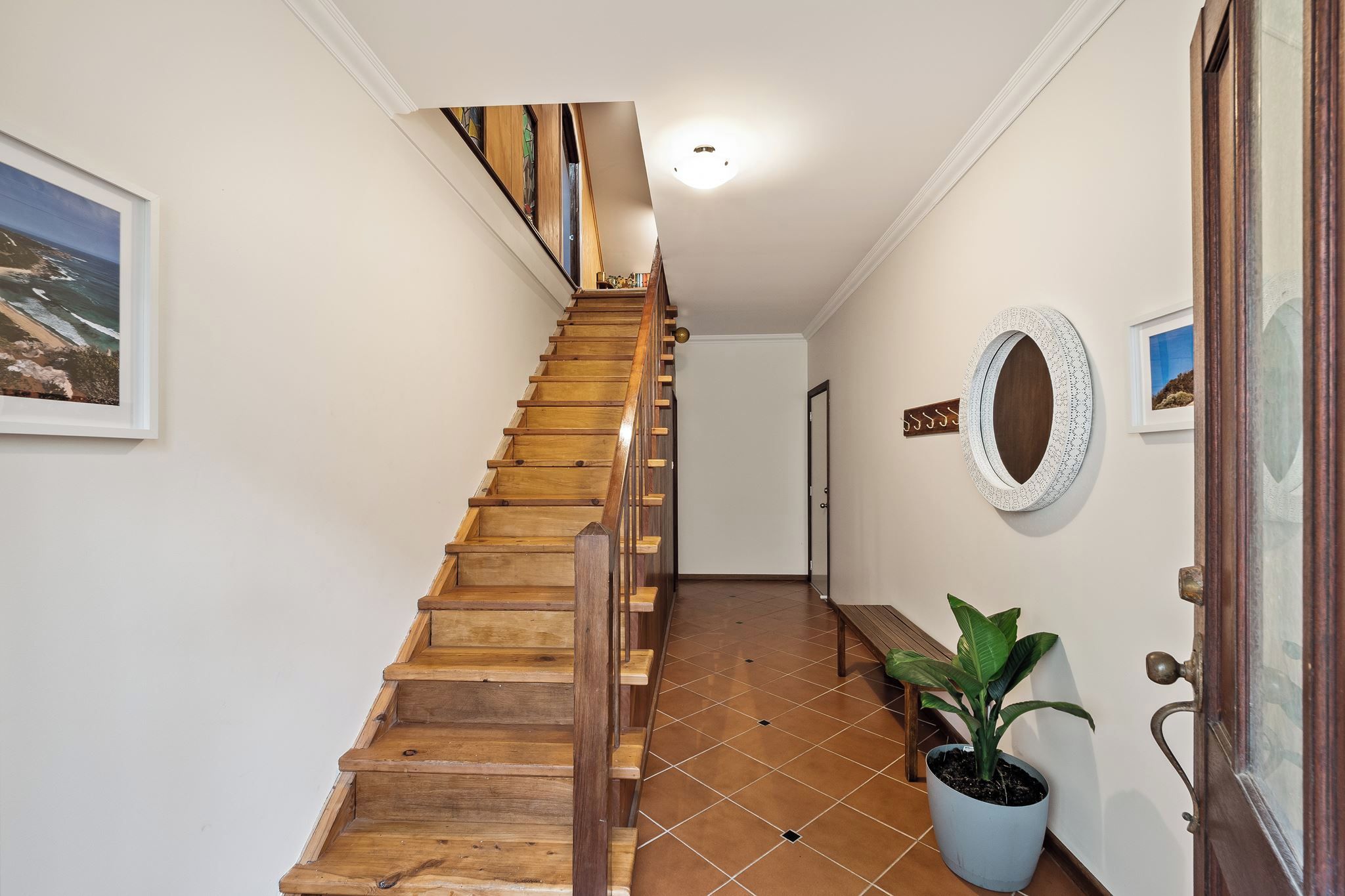 Un escalier en bois mène à un palier où se trouvent une plante en pot et un miroir accroché au mur.