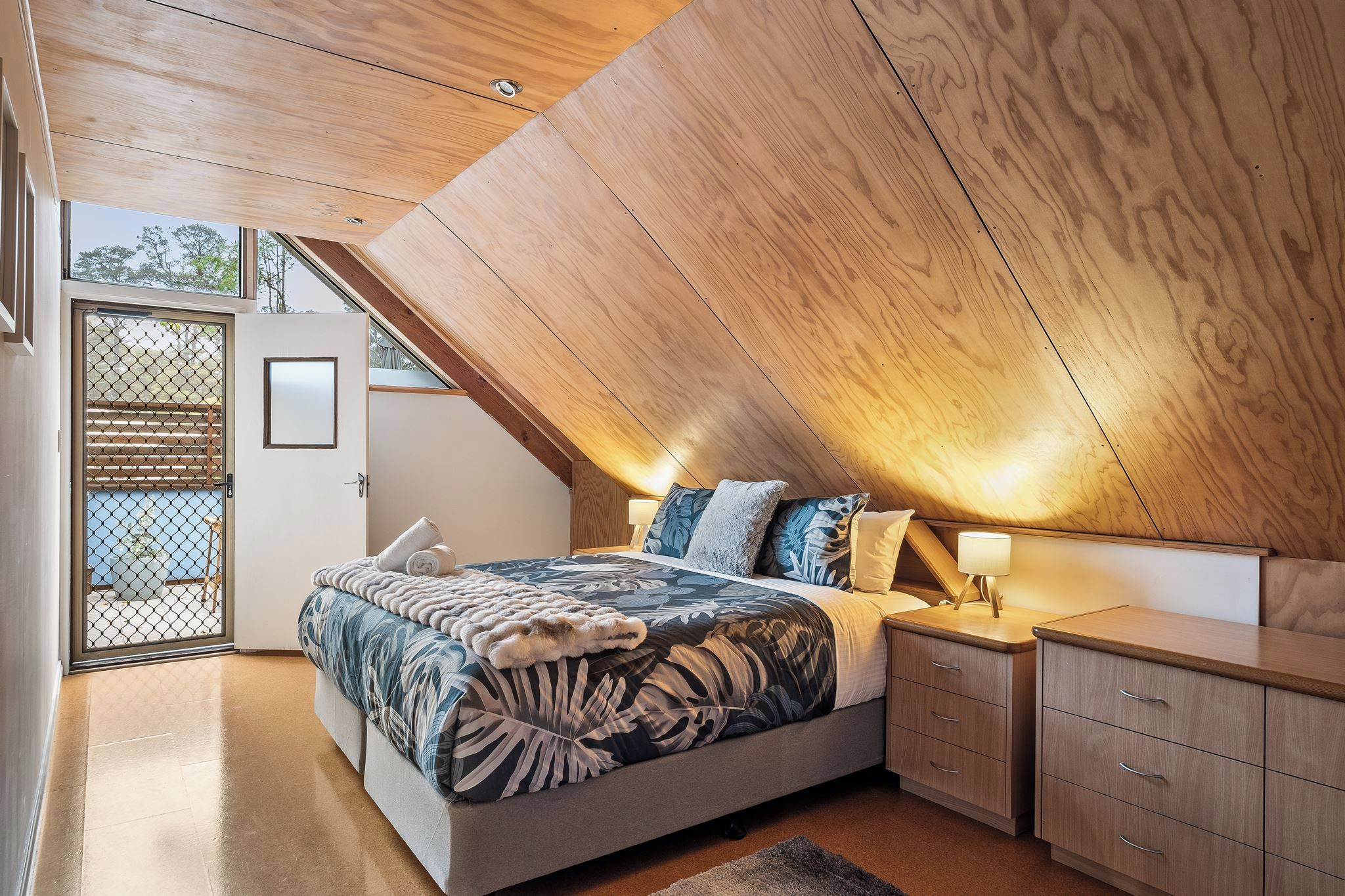 A bedroom with a sloped ceiling, a bed with patterned bedding, bedside tables, and a view through a door.