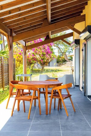 Eine Terrasse im Freien mit einem Holztisch und -stühlen, einem kleinen runden Tisch und einem überdachten Bereich mit einer Pergola.