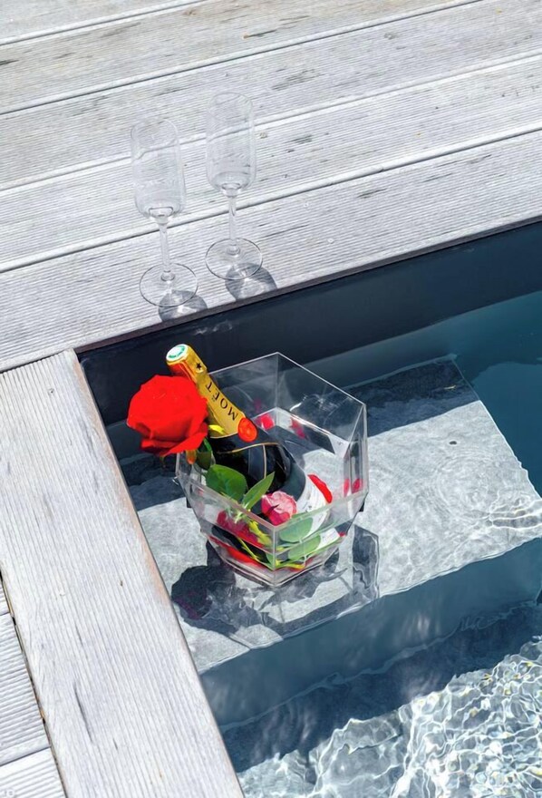 Ein Glasgefäß mit einer Flasche und einer Rose auf einem Holzdeck an einem Pool.