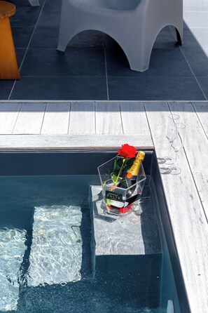 A pool area with a clear water surface, a glass container with a bottle and a red rose, and white plastic chairs in the background. - Sahari: 3-bedroom apartment with private pool, centrally located and quiet (Les Abymes)