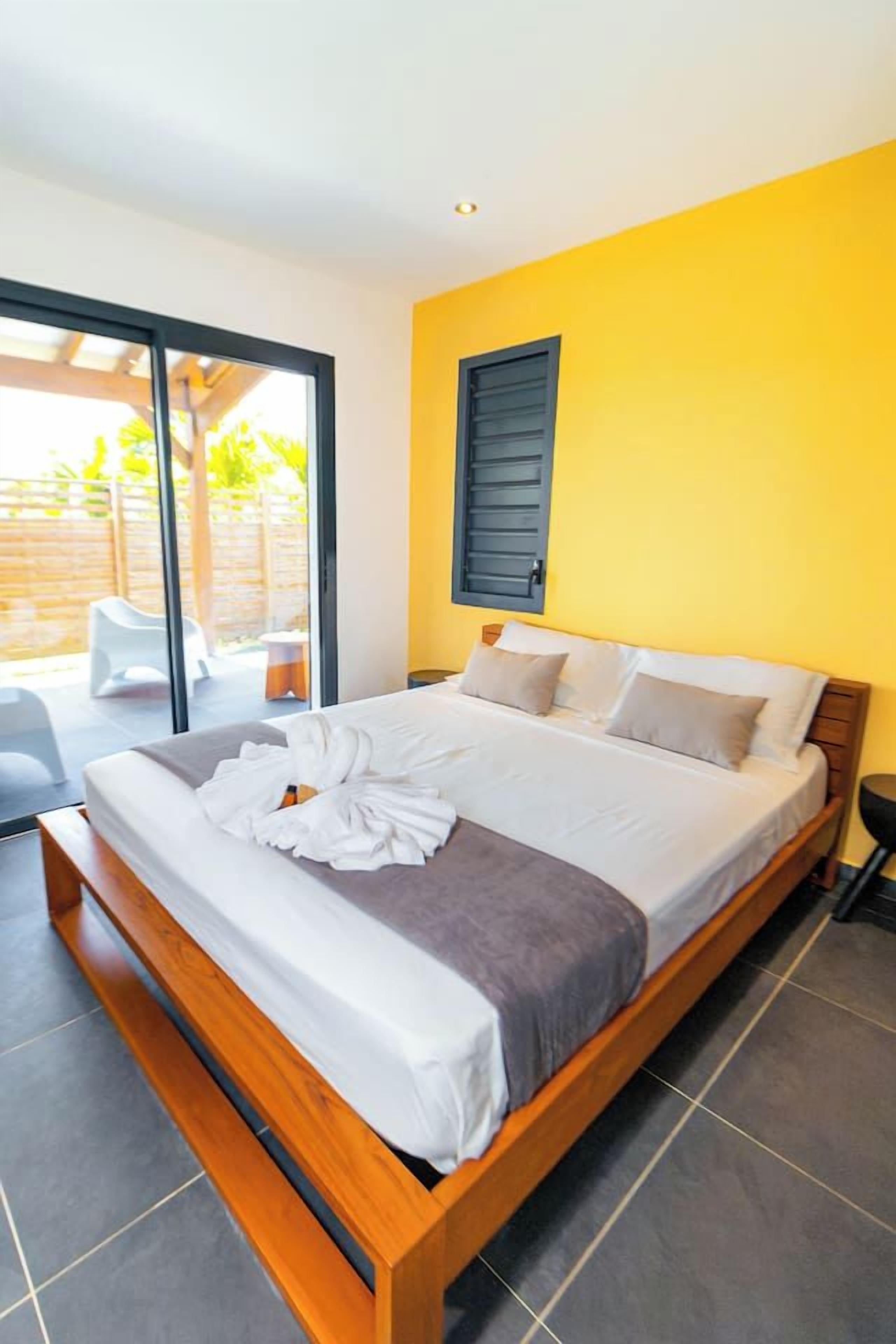 Ein modernes Schlafzimmer mit einem großen Bett, einer Schiebeglastür zu einer Terrasse und einer strahlend gelben Wand.