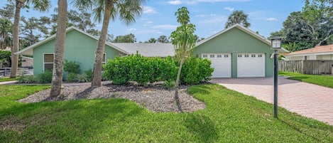 A residential property with a green house, two garage doors, and a well-maintained lawn.