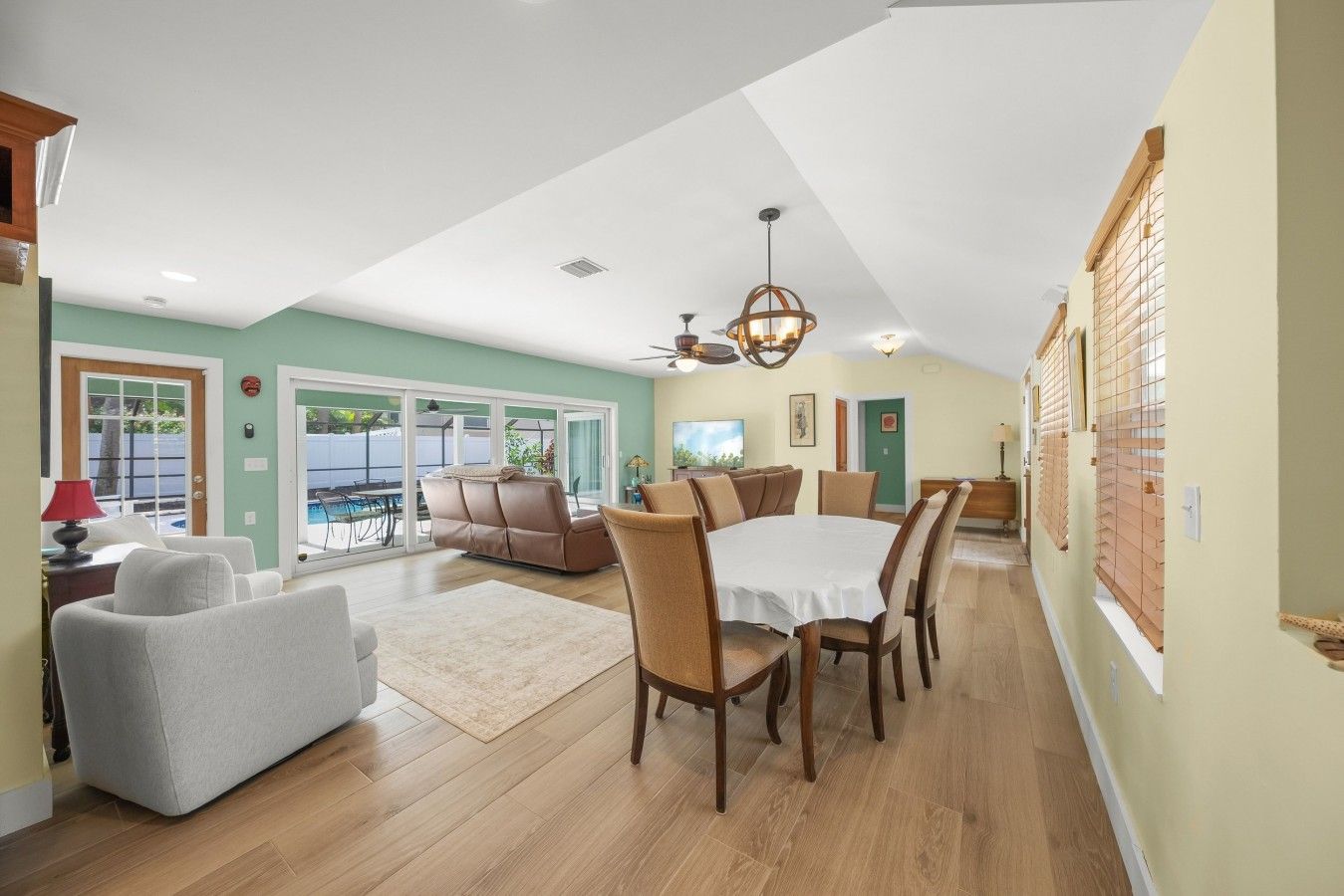 A spacious living area with a dining table, sofas, and a view of a pool.