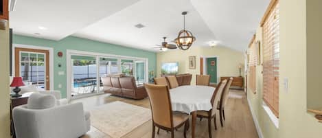 A spacious living area with a dining table, sofas, and a view of a pool.