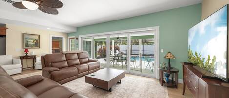 A living room with a brown leather sofa, a coffee table, a flat-screen TV, and a ceiling fan.