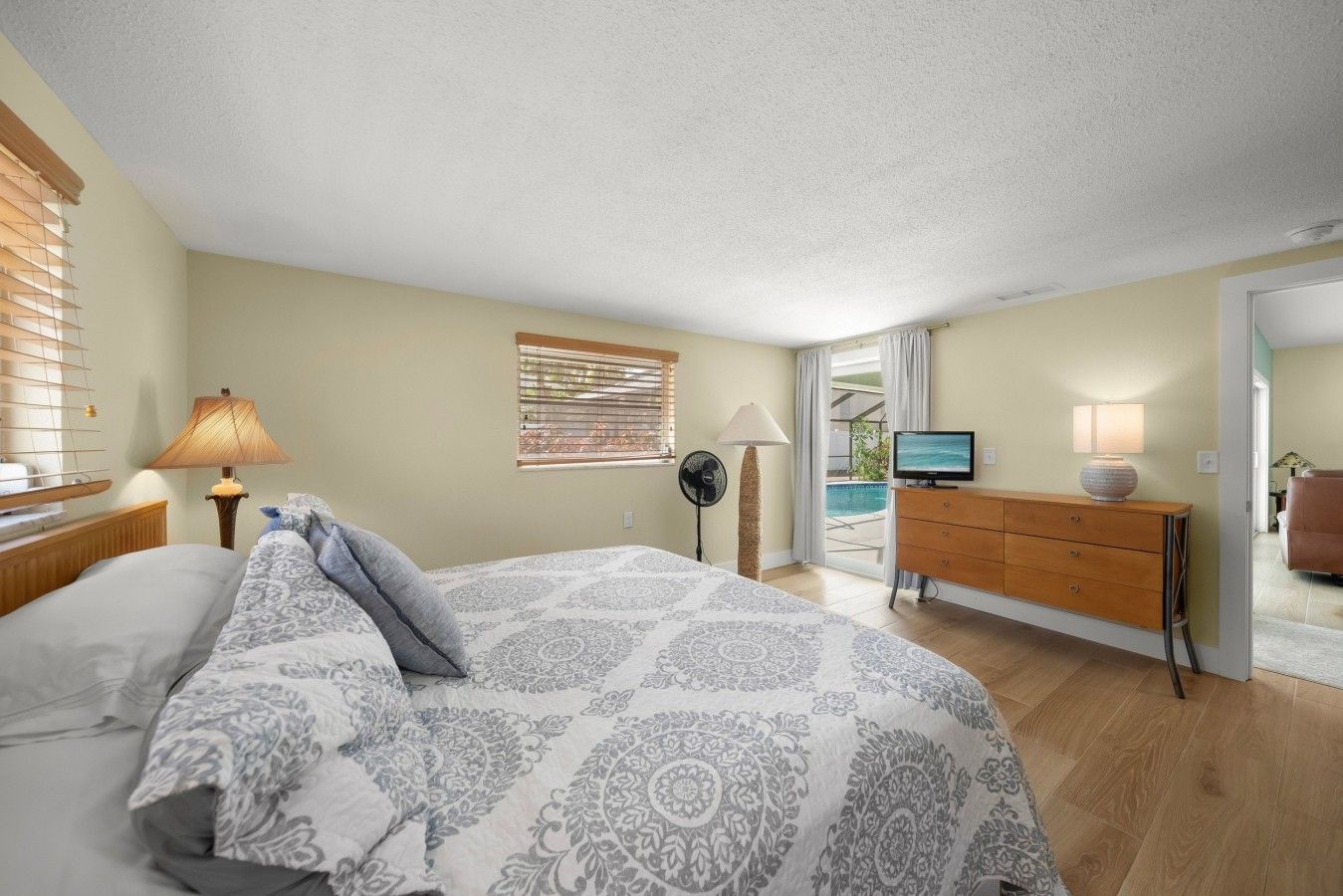 Une chambre à coucher comprenant un lit, une commode, un téléviseur et une fenêtre avec des stores.