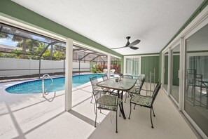Un espace extérieur abrité comprenant une piscine, une table avec des chaises et un ventilateur de plafond.