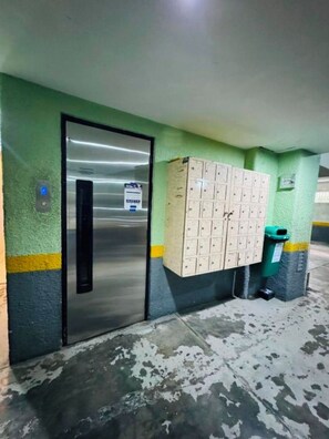 Eine Parkgarage mit einer Metall-Aufzugstür, einer Reihe von Schließfächern und einem Mülleimer.