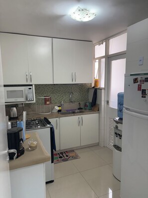 A kitchen with white cabinets, a microwave, a gas stove, a water dispenser, and a refrigerator. - Fantastic 3-bedroom apartment with AC in vibrant Rio de Janeiro (Rio de Janeiro)