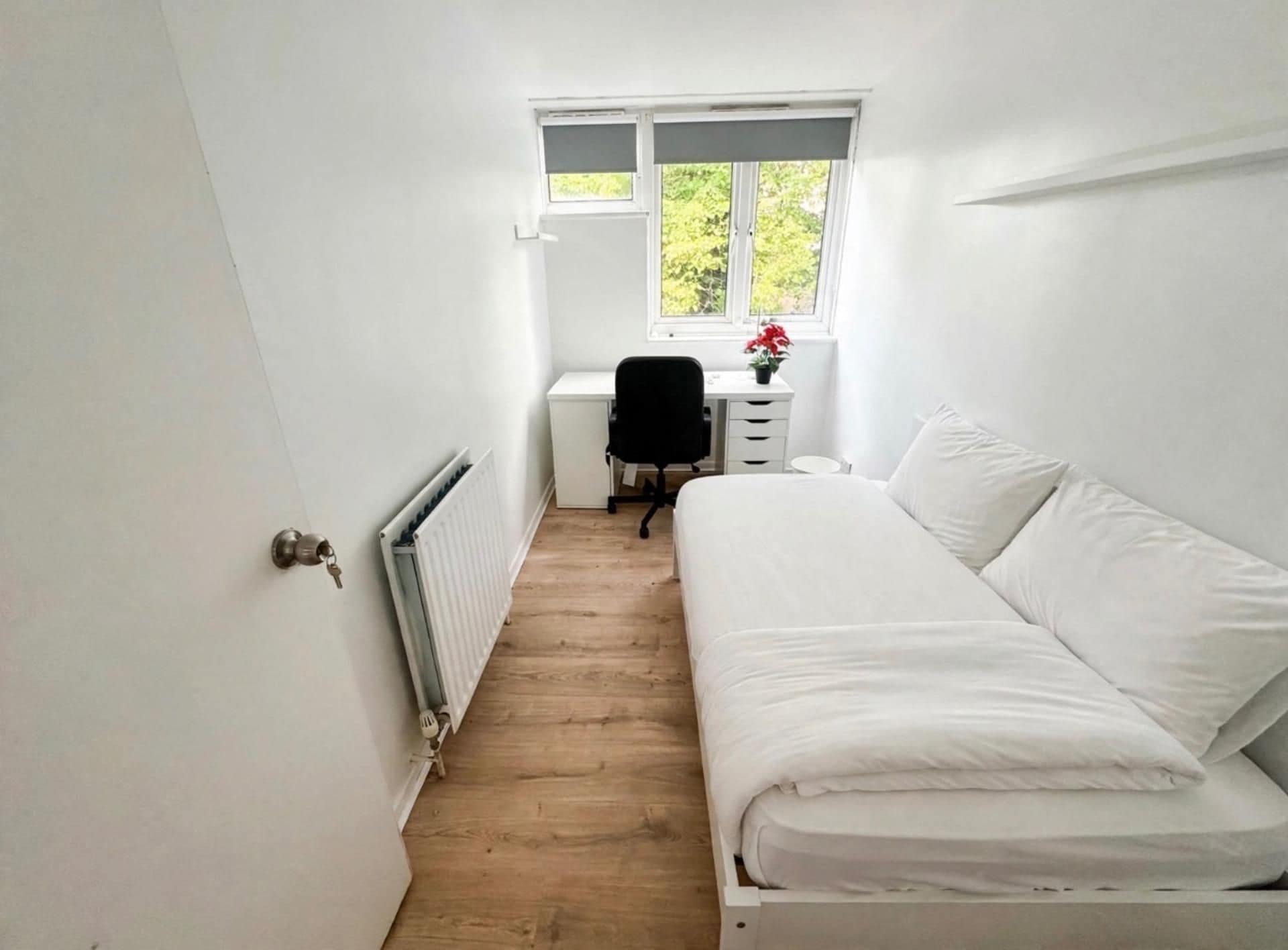 A narrow room with a bed, a desk, and a radiator.