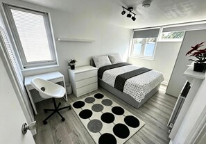 Un dormitorio con cama, mesita de noche, silla y ventana.
