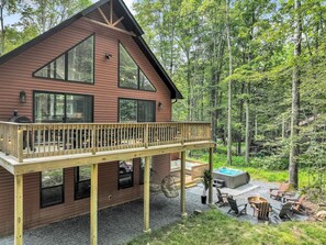 A cabin with a deck, hot tub, and outdoor seating area surrounded by trees. - Hot Tub, Luxe, Game Room, Open Concept, Privacy (Tobyhanna Township)