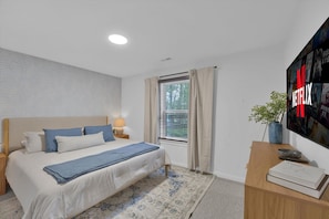 A bedroom with a bed, bedside table, lamp, window with curtains, and a wall-mounted TV. - Hot Tub, Luxe, Game Room, Open Concept, Privacy (Tobyhanna Township)