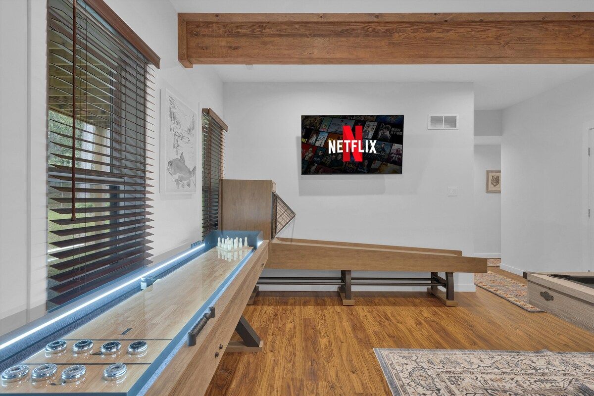 Ein modernes Wohnzimmer mit einem Holztisch, einem Schachbrett und einem an der Wand befestigten Fernseher, der das Netflix-Logo zeigt.