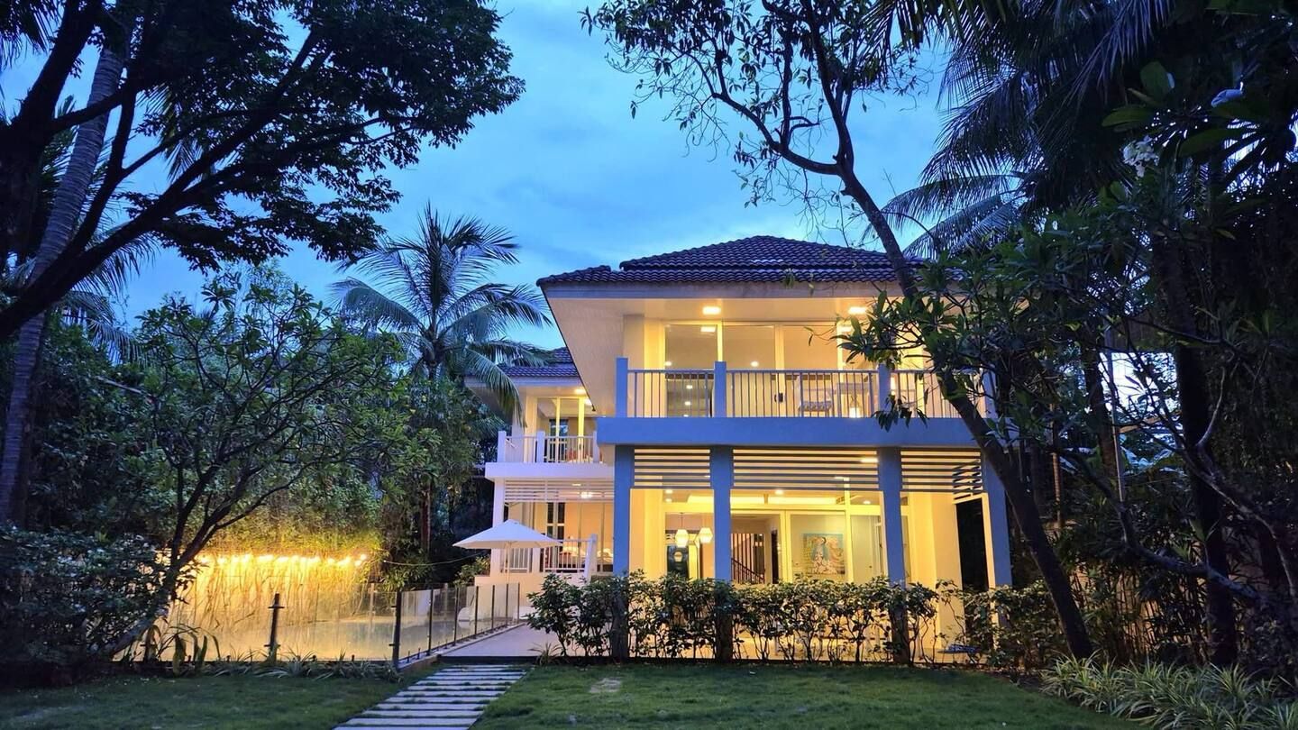 A two-story house with a balcony, surrounded by lush greenery and a well-maintained lawn.