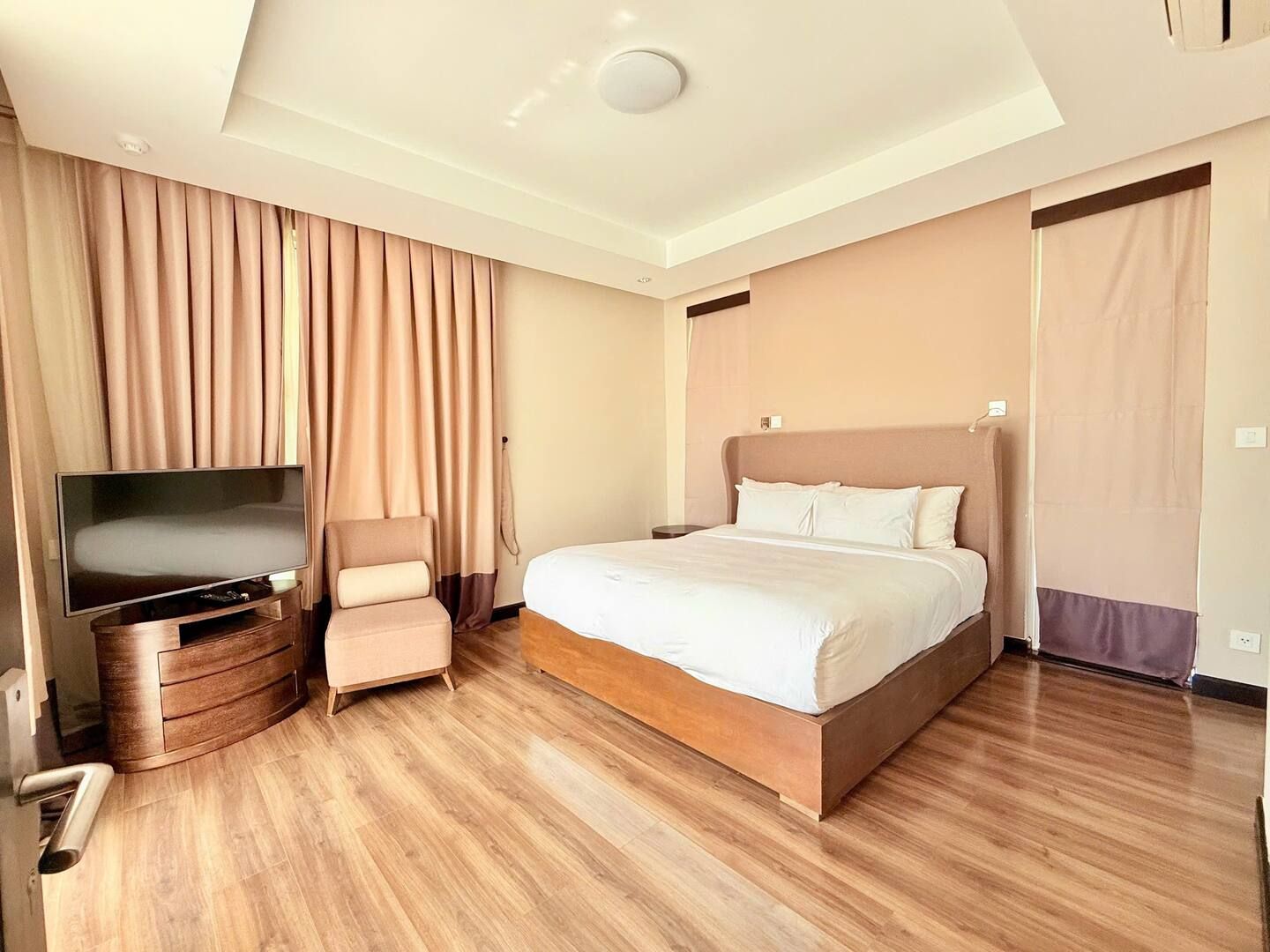 A hotel room with a bed, a TV, a chair, and a wooden floor.