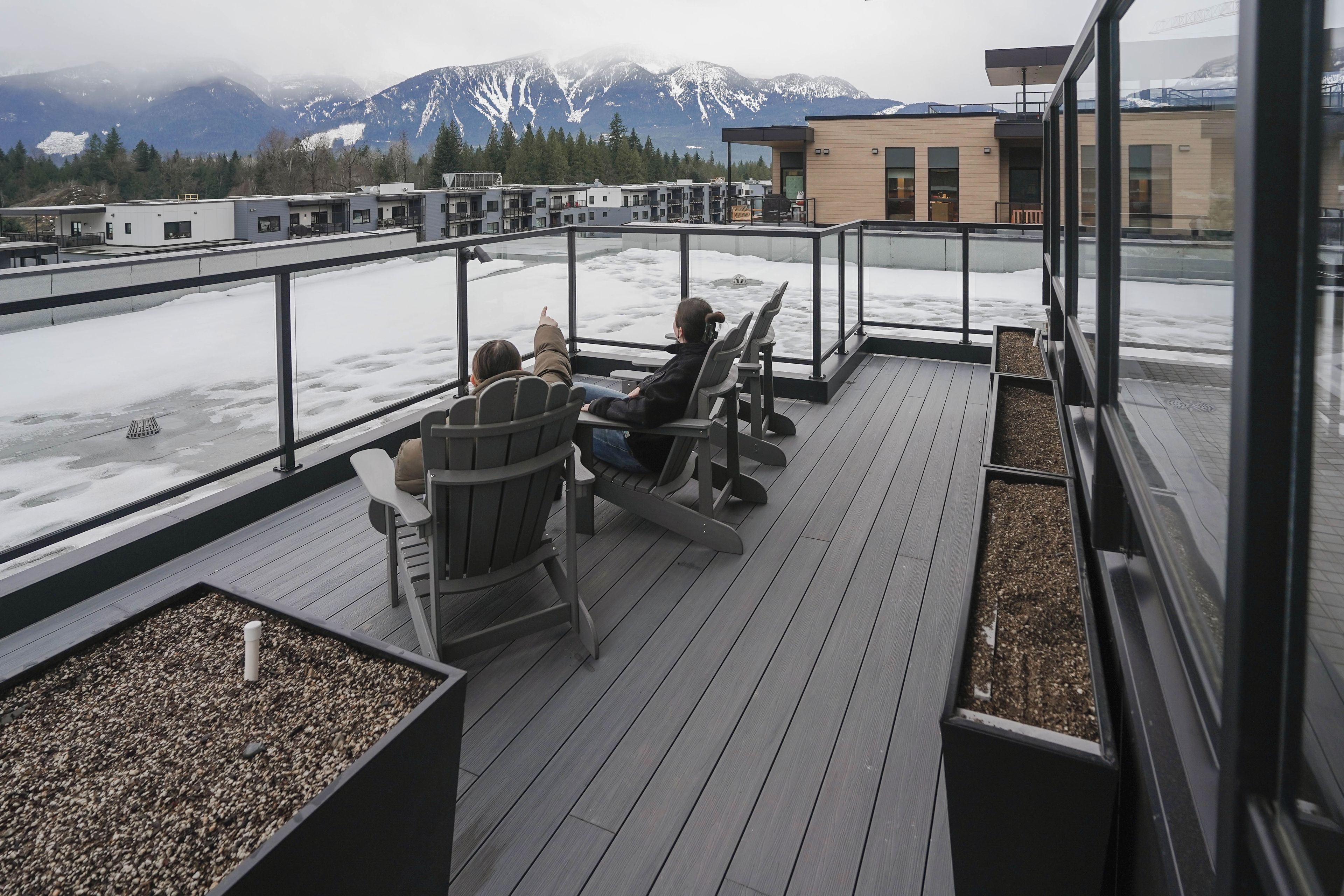 A rooftop terrace with seating, a view of snow-covered mountains, and a modern building in the background.