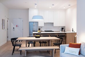 Eine moderne Küche mit weißen Schränken, einer zentralen Kochinsel und einem Essbereich mit einem Holztisch und Stühlen.