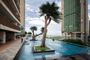 Ein Swimmingpool mit Palmen, ein Restaurantbereich und hohe Gebäude im Hintergrund.