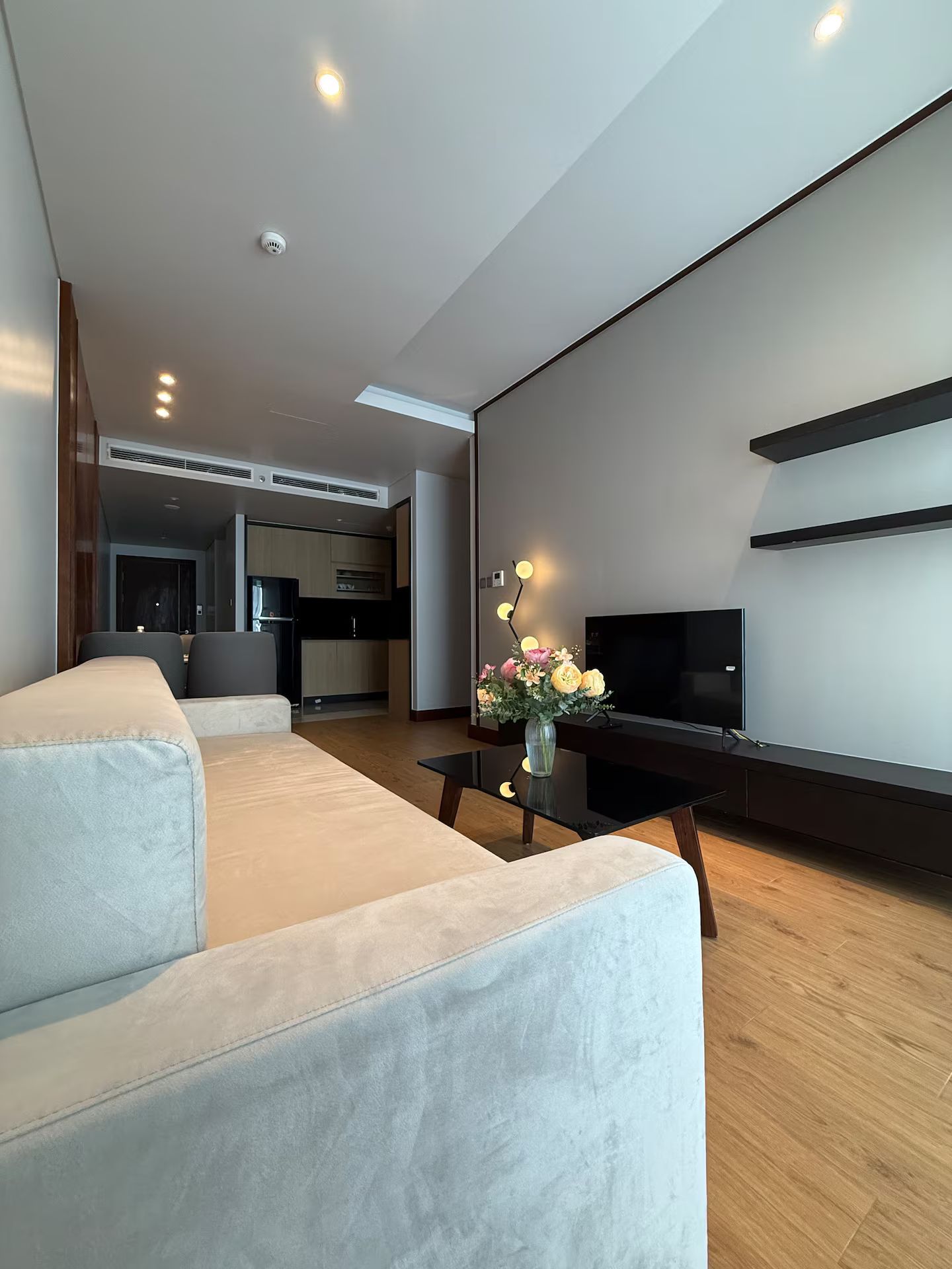 A modern living room with a sofa, a coffee table, a TV, and a vase with flowers.