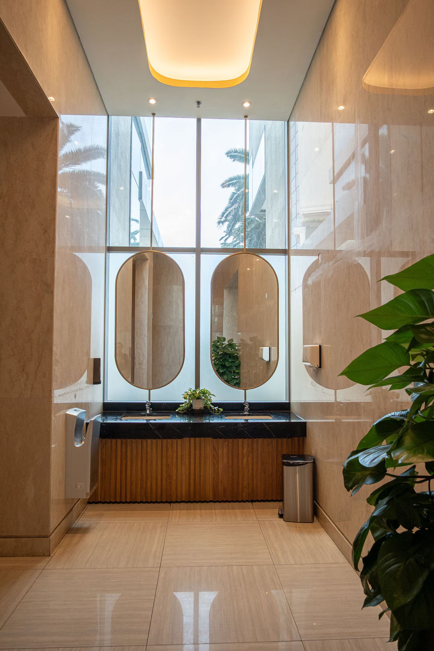 A modern bathroom with a large mirror, a sink, and a trash bin.