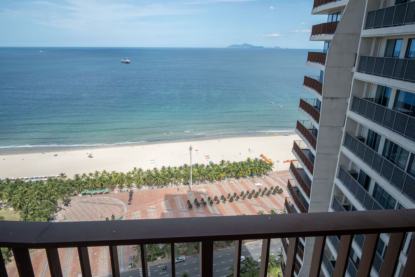 A beach view from a balcony overlooking a sandy beach with palm trees and a clear sky.