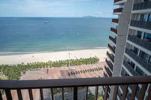 Blick auf einen Strand von einem Balkon mit Palmen und blauem Himmel.