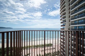 Ein Balkon mit Blick auf Strand und Meer, ein Hochhaus mit mehreren Balkonen und ein klarer Himmel.