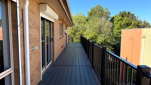 Une terrasse en bois avec une rambarde noire, un bâtiment en briques et un ciel dégagé.