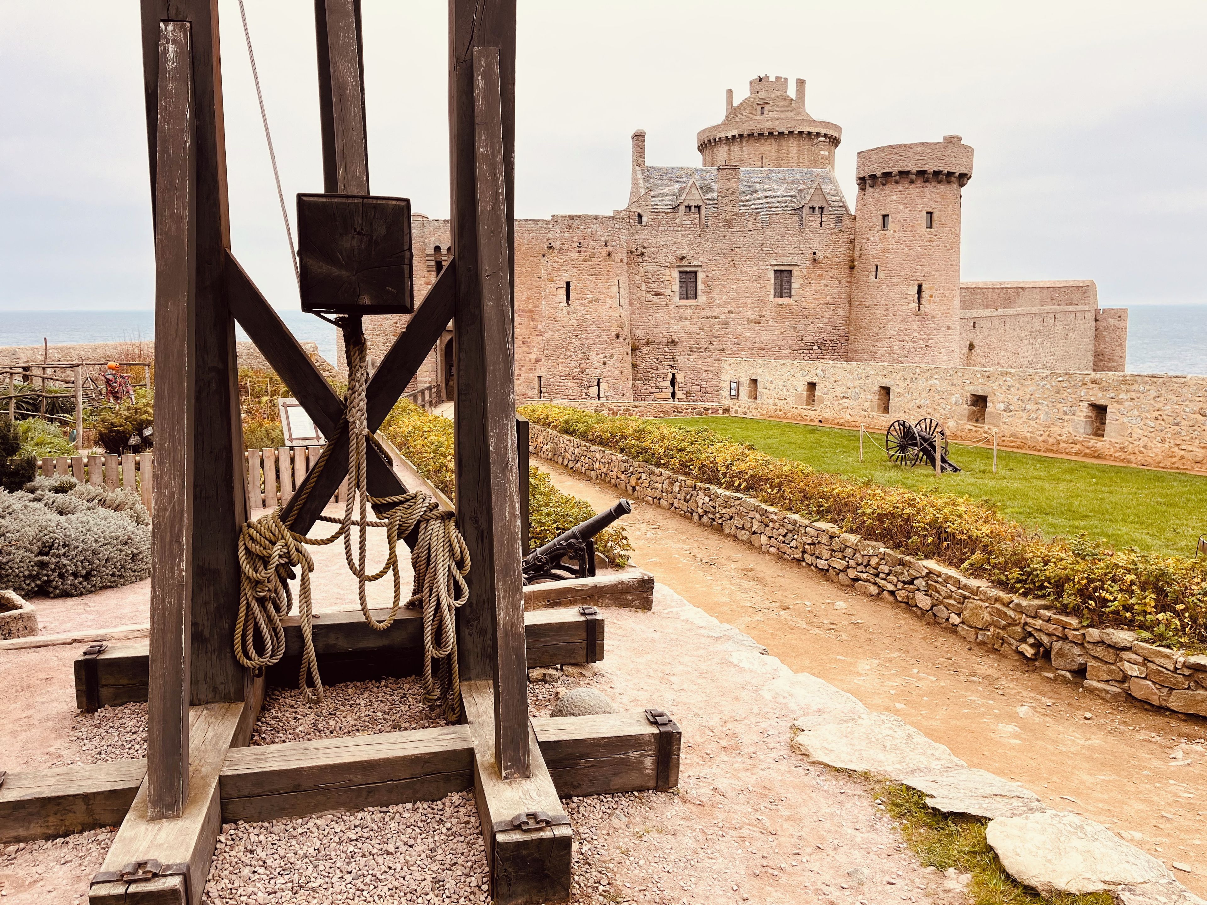 Un castillo histórico con un puente levadizo, muros de piedra y una zona verde.