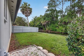 A residential backyard with a lawn, a small pond, and a wooden fence. - Players Club Getaway I Sawgrass (Palm Valley)
