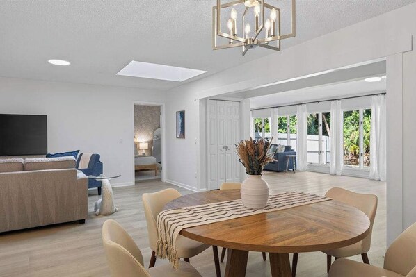 A modern living room with a sofa, a dining table with chairs, and a TV.