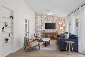 Un salon comprenant un canapé, des fauteuils, une table basse, un téléviseur fixé au mur et une bibliothèque.