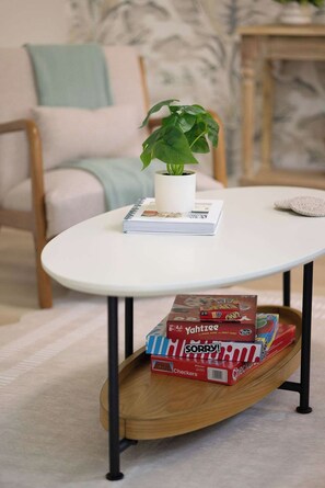 Uma mesa branca com uma planta em vaso, um livro e uma pilha de jogos de tabuleiro.