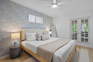 A bedroom with a bed, bedside lamps, a ceiling fan, and a window with blinds.