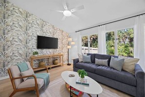 A living room with a sofa, armchair, coffee table, and a TV mounted on the wall.