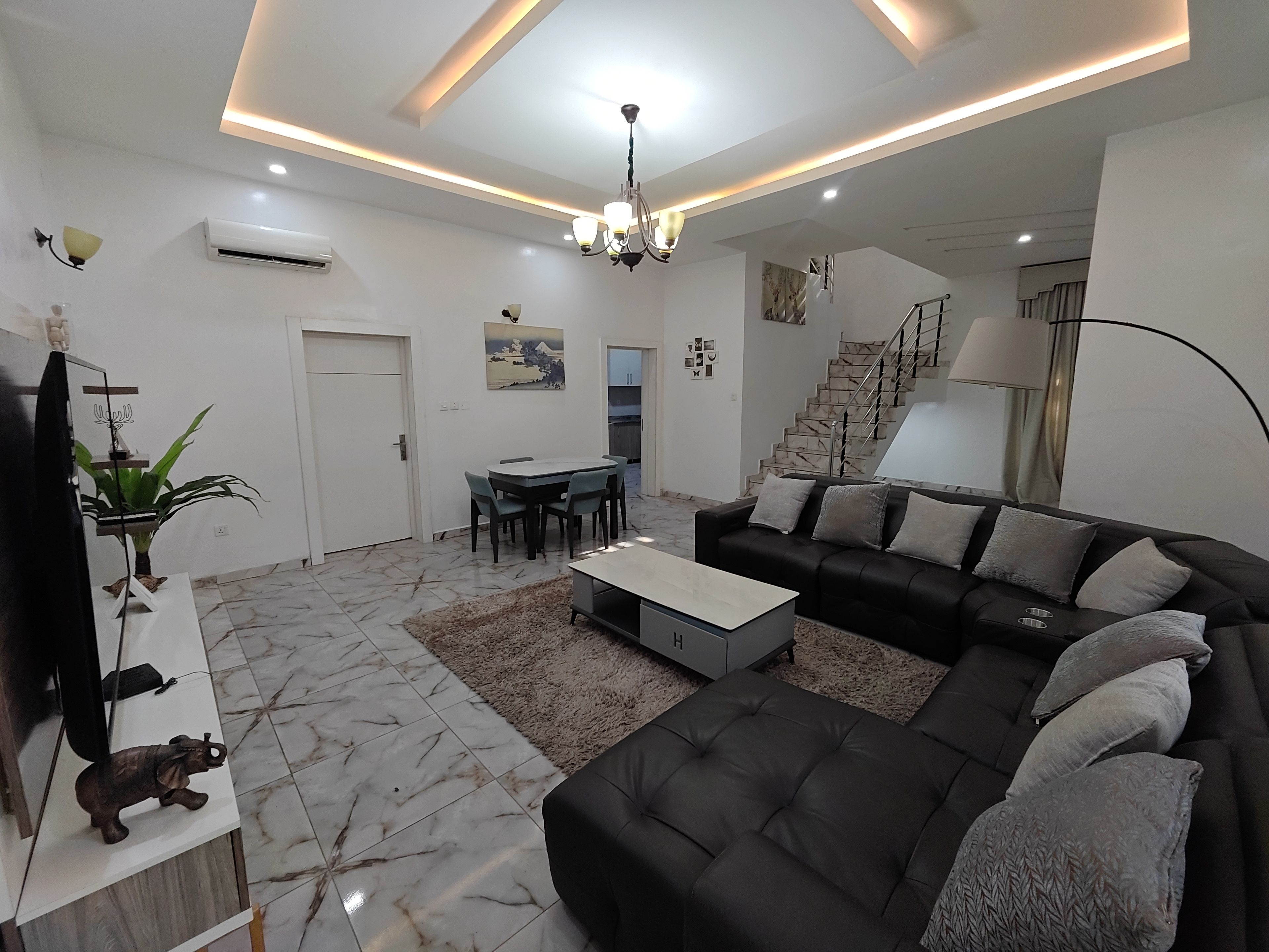 A modern living room with a black sofa, a dining table, and a staircase.