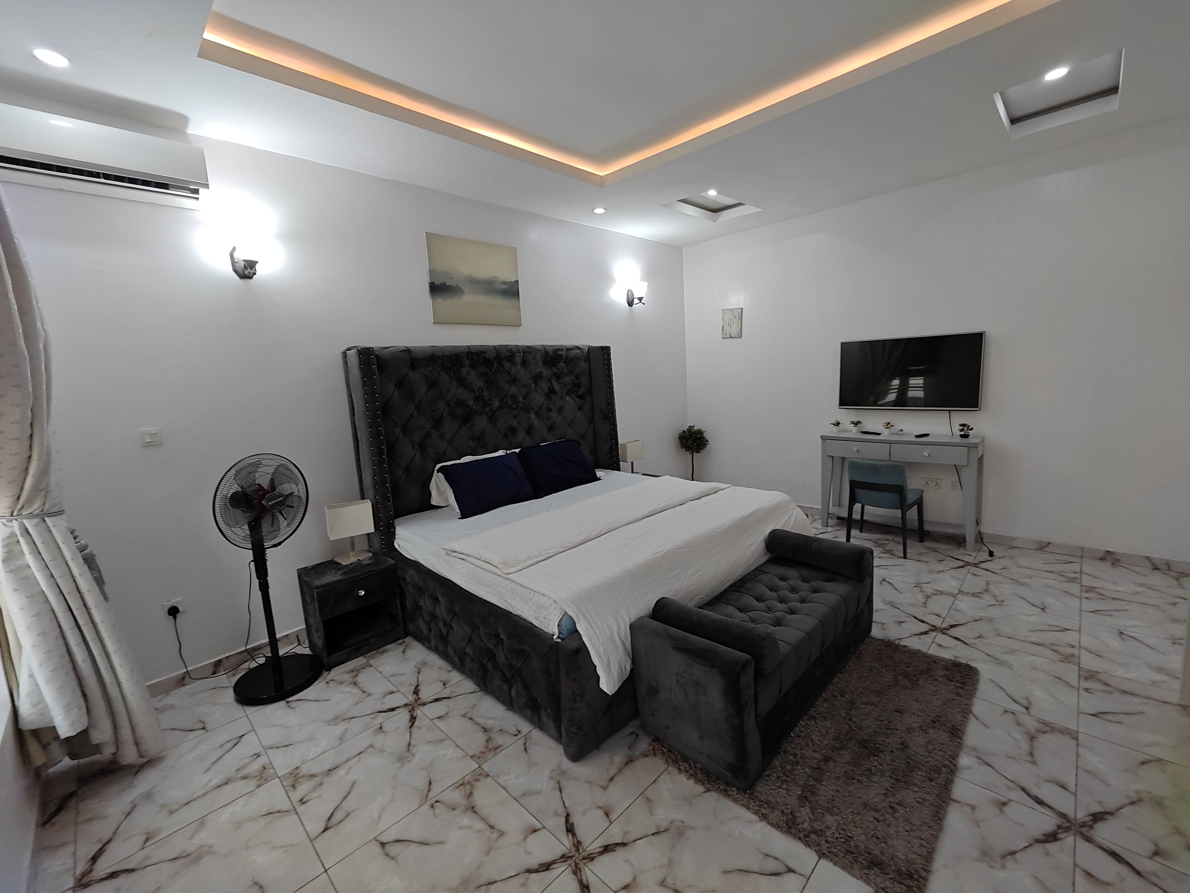 Un dormitorio moderno con una cama grande, mesitas de noche, un escritorio y una televisión.