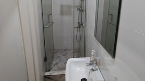 Ein Badezimmer mit einer Duschkabine aus Glas, einem weißen Waschbecken und einem Spiegel.