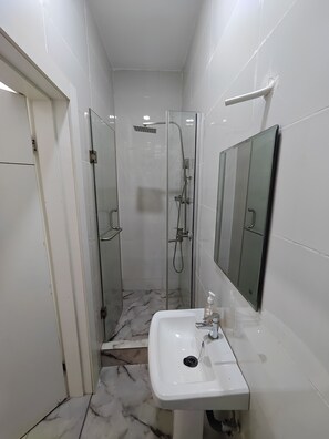 Une salle de bain avec une douche à parois de verre, un lavabo blanc et un miroir.