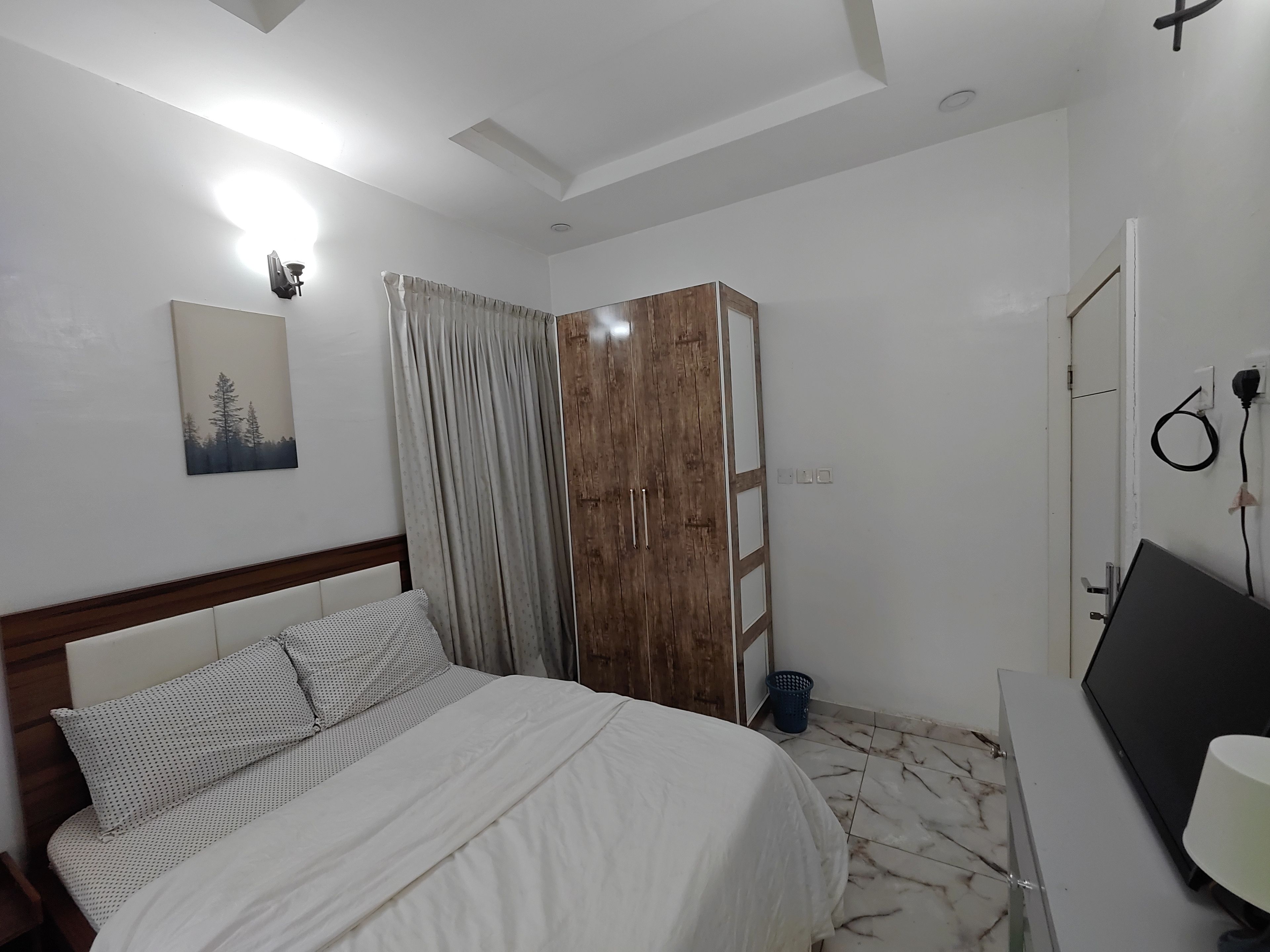Ein Schlafzimmer mit einem Bett, einem Kleiderschrank, einem Schreibtisch und einer Wandleuchte.